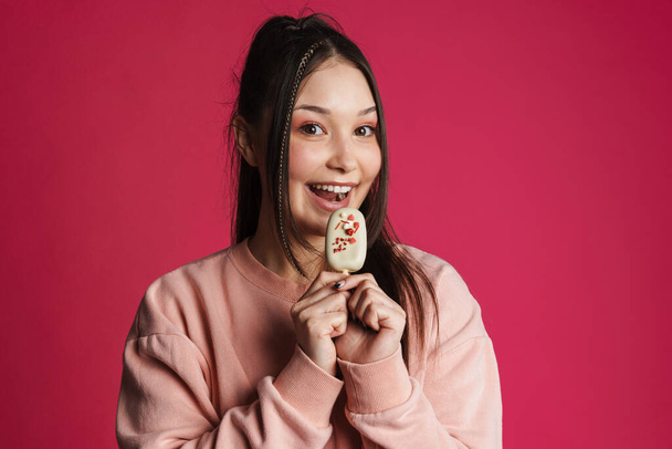 Asian brunette happy woman smiling while eating ice cream isolated over purple wall - Foto, afbeelding