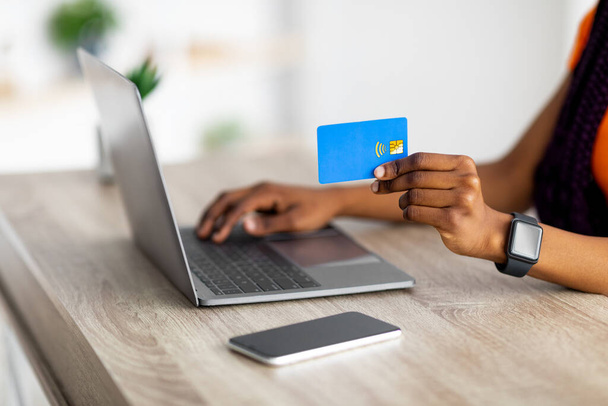 Крупним планом чорна жінка тримає кредитну картку і використовує ноутбук, робить електронні платежі на комп'ютері, купує онлайн з дому
 - Фото, зображення