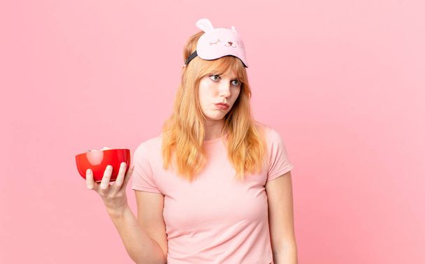pretty red head woman feeling sad, upset or angry and looking to the side wearing pajamas and holding a flakes bowl - Fotoğraf, Görsel
