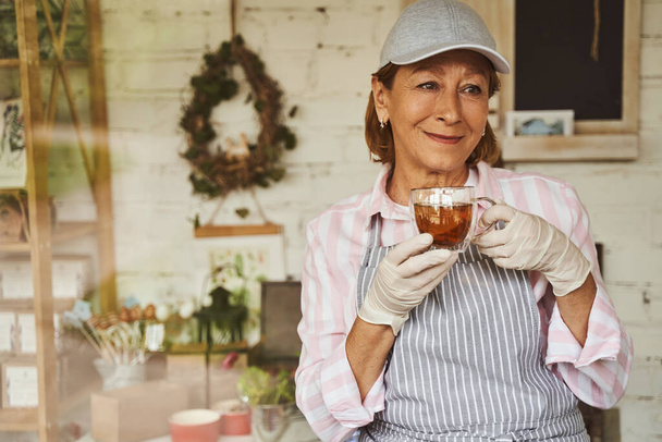 Happy florist relaxing with hot drink in shop - Foto, Imagem