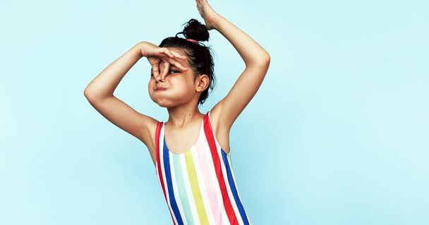 Playful little girl holding her nose for swimming poses indoor against a blue background. A cute small girl in colorful swimwear holding her nose to learning to swim in the pool. - 写真・画像