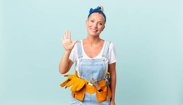pretty blond woman smiling and looking friendly, showing number five and repairing house concept - Foto, Bild