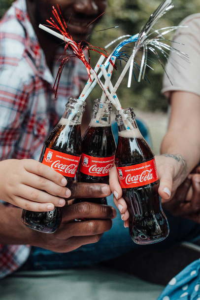 Gehakt deel van de familie met flessen cola met rietjes tijdens de picknick in het park  - Foto, afbeelding