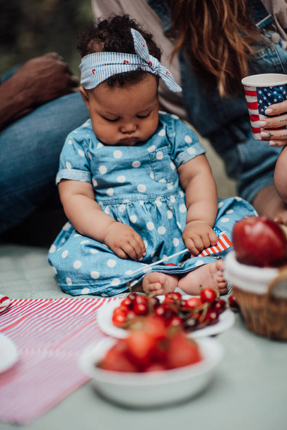Sección recortada de la madre sentada con una niña sosteniendo cerezas rojas y bandera estadounidense - Foto, Imagen
