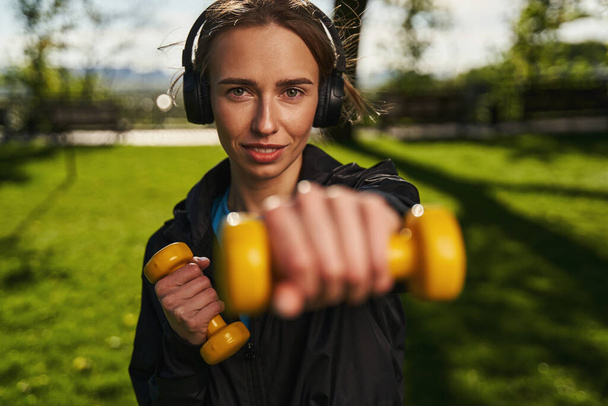 Fröhliche Frau trainiert Arme mit Gewichten im Freien - Foto, Bild