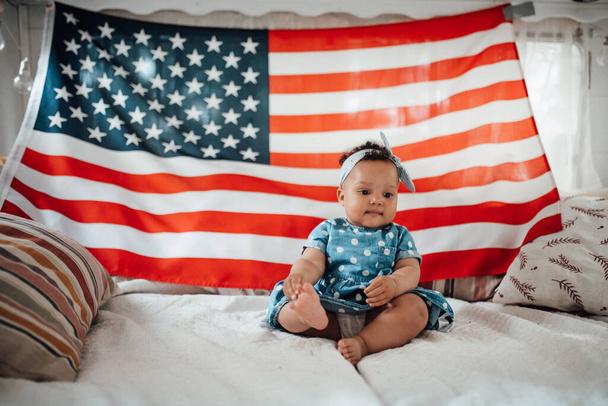 Bella bambina in abito blu seduta sul divano con sfondo bandiera americana   - Foto, immagini