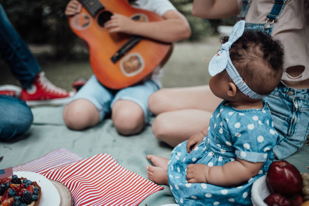 Portrét malé holčičky při pikniku v parku, rozmazané rodinné pozadí  - Fotografie, Obrázek