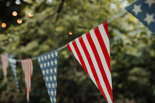 Πολύχρωμες σημαίες σε αμερικανικό στυλ κρεμασμένα σε σχοινί, θολή φόντο πάρκο  - Φωτογραφία, εικόνα