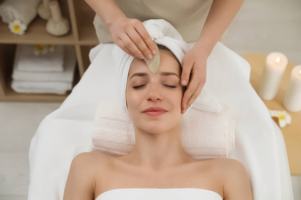 Young woman receiving facial massage with gua sha tool in beauty salon - Фото, изображение