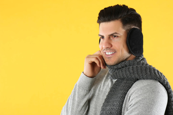 Man wearing stylish earmuffs and scarf on yellow background. Space for text - Foto, immagini