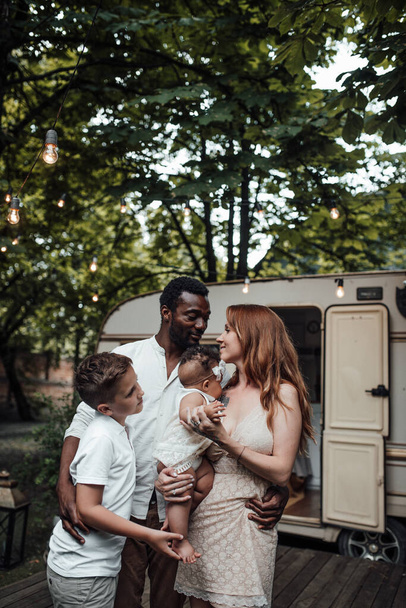 Outdoor portrait of happy family standing in park with trailer on background - Photo, Image