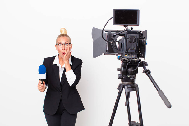 pretty blond woman feeling shocked and scared and holding a pmicrophone. presenter concept - Φωτογραφία, εικόνα