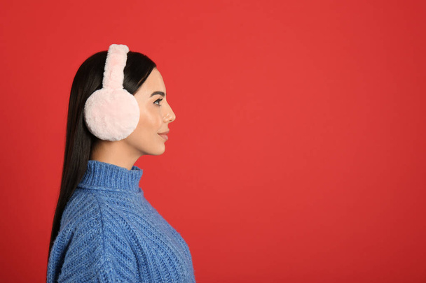 Beautiful young woman wearing earmuffs on red background. Space for text - Foto, immagini