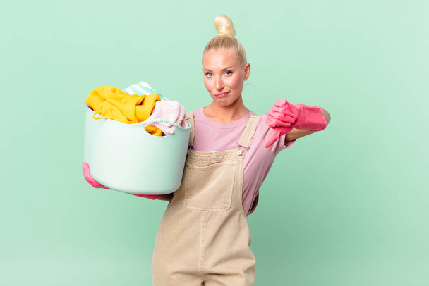 pretty blond woman feeling cross,showing thumbs down washing clothes concept - Фото, изображение
