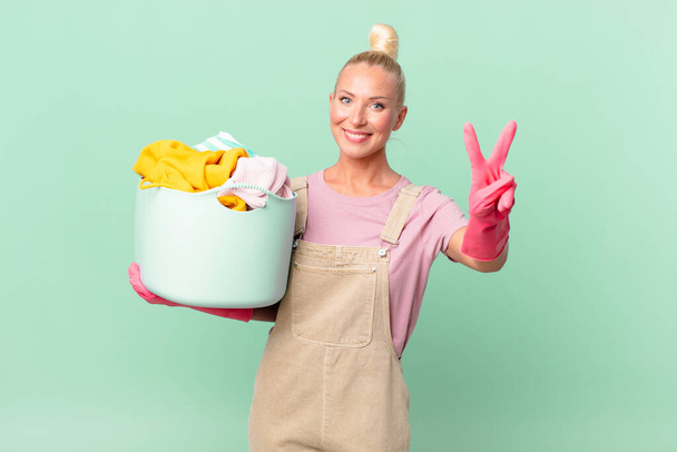 pretty blond woman smiling and looking friendly, showing number two washing clothes concept - Fotó, kép