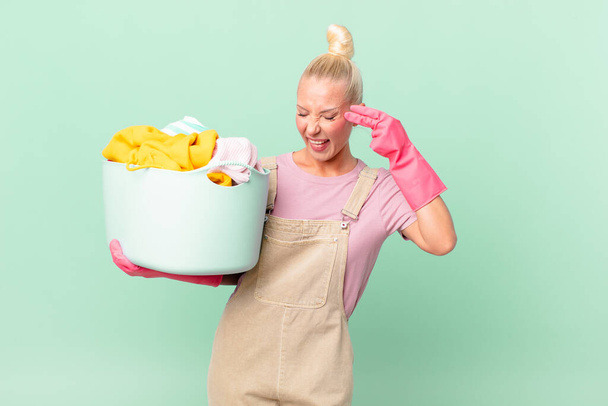 pretty blond woman looking unhappy and stressed, suicide gesture making gun sign washing clothes concept - Photo, Image