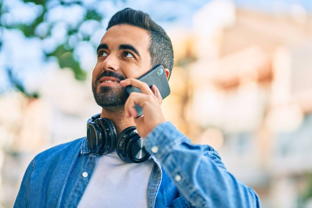 Young hispanic man smiling happy talking on the smartphone at the city. - 写真・画像