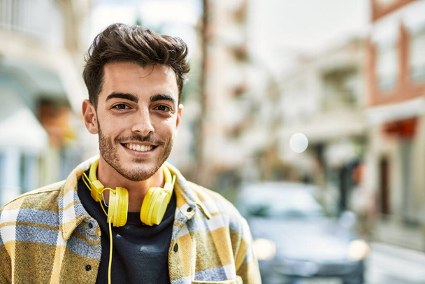 bel homme hispanique souriant heureux et confiant à la ville portant des écouteurs avec un style moderne - Photo, image