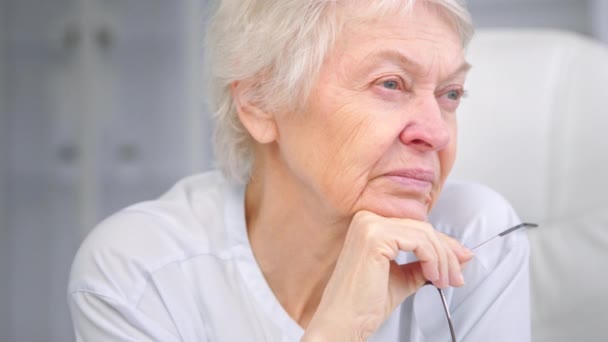 Senior γιαγιά με κοντά γκρίζα μαλλιά κατέχει γυαλιά - Πλάνα, βίντεο