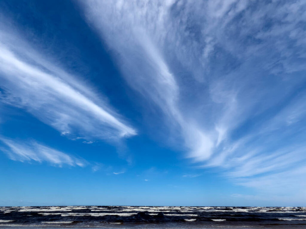 Erős szél fúj az égen a tenger felett, hullámok és homályos fehér felhők - Fotó, kép