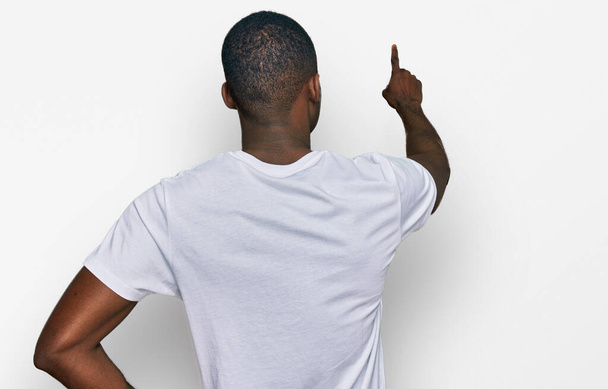 Beyaz bir tişört giyen genç Afro-Amerikan bir adam tersten parmağıyla öne doğru poz veriyor.  - Fotoğraf, Görsel