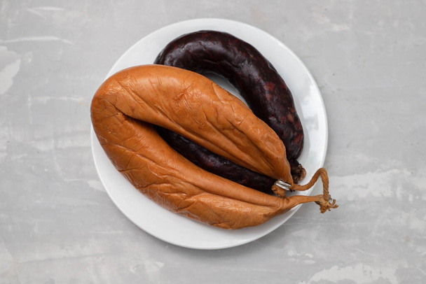 two smoked sausages on white small dish on ceramic background - Foto, Imagen