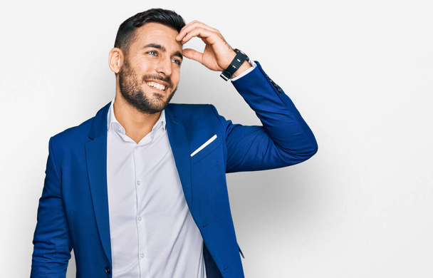Молодий іспаномовний чоловік в діловому піджаку посміхається впевнено торкаючись волосся ручним жестом, позує привабливо і модно
  - Фото, зображення