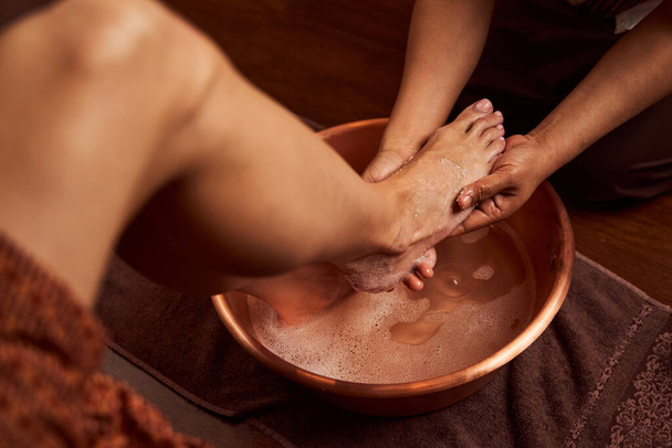 Experienced chiropodist washing foot in special container in spa salon - 写真・画像