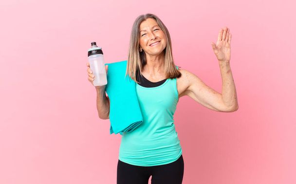 pretty middle age woman smiling happily, waving hand, welcoming and greeting you. fitness concept - Zdjęcie, obraz