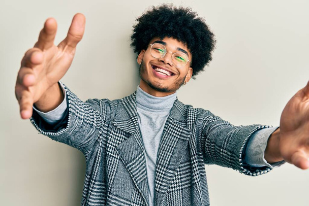 アフリカ系アメリカ人の若い男性は、カメラを見てカジュアルな服の眼鏡を着用し、抱擁のために腕を開いて笑顔。幸せを受け入れる陽気な表情.  - 写真・画像