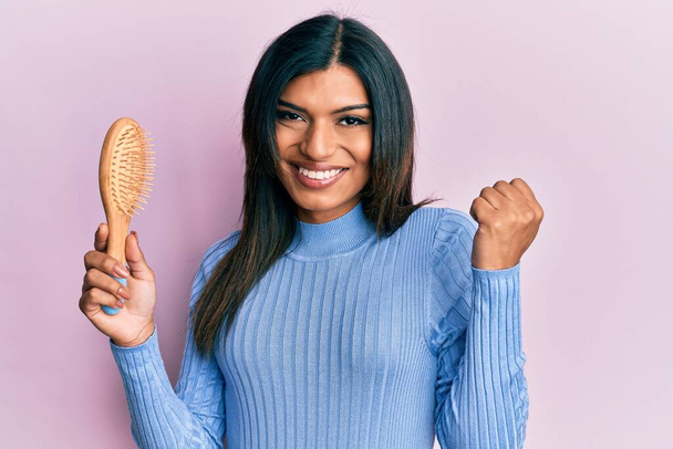 Young latin transsexual transgender woman holding hairbrush screaming proud, celebrating victory and success very excited with raised arm  - Foto, Imagem