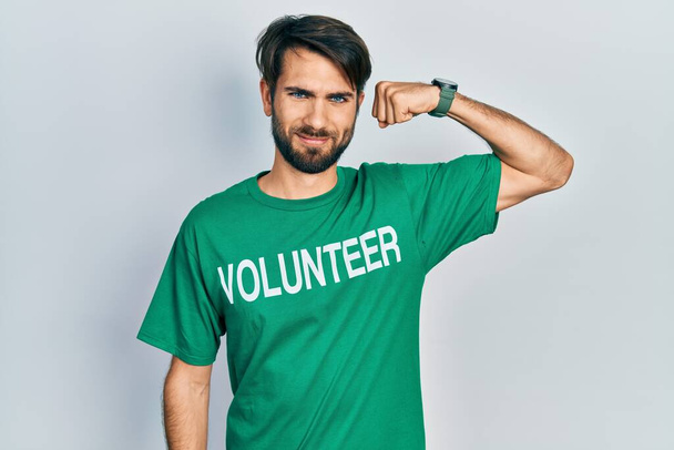 Junger hispanischer Mann im freiwilligen T-Shirt starke Person, die Armmuskeln zeigt, selbstbewusst und stolz auf die Macht  - Foto, Bild