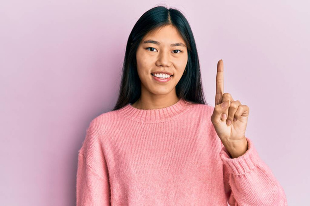 Giovane donna cinese che indossa abiti casual sorridente con un'idea o una domanda puntando il dito verso l'alto con la faccia felice, numero uno  - Foto, immagini