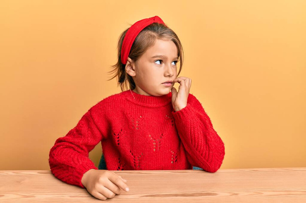 Little beautiful girl wearing casual clothes sitting on the table looking stressed and nervous with hands on mouth biting nails. anxiety problem.  - Photo, Image