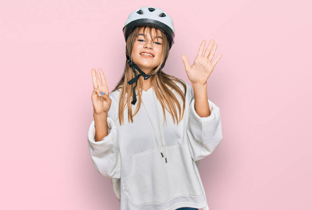 Adolescente chica caucásica con casco de bicicleta mostrando y apuntando hacia arriba con los dedos número ocho mientras sonríe confiado y feliz.  - Foto, imagen