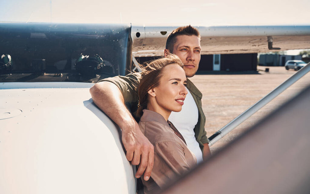 Όμορφο νεαρό ζευγάρι στέκεται δίπλα σε αεροσκάφη στο αεροδρόμιο - Φωτογραφία, εικόνα