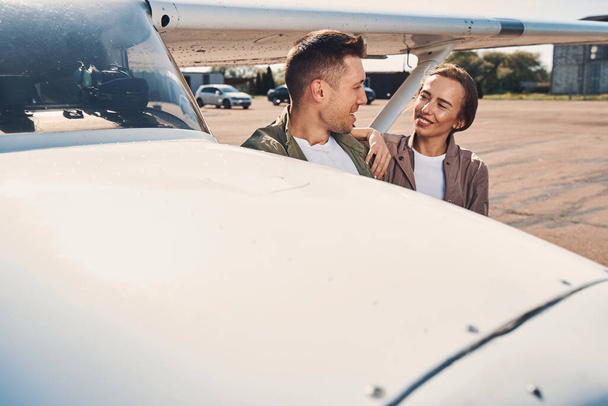 Beautiful happy couple standing by aircraft at airfield - Фото, изображение