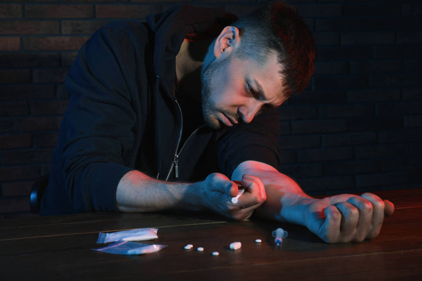 Addicted man taking drugs at table indoors - Photo, image