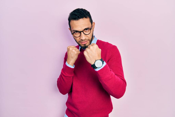 Hispanic man with beard wearing business shirt and glasses ready to fight with fist defense gesture, angry and upset face, afraid of problem  - Foto, Imagem