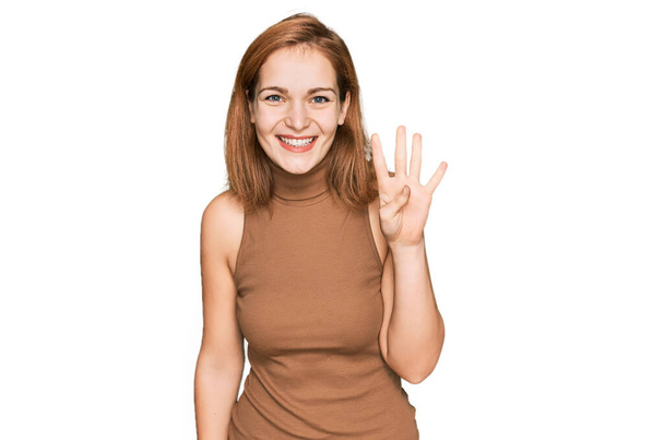Młoda kaukaska kobieta w luźnych ubraniach pokazuje i wskazuje palcami numer cztery, uśmiechając się pewny siebie i szczęśliwy.  - Zdjęcie, obraz