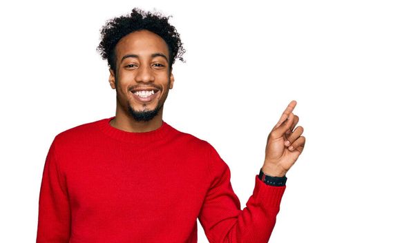 Young african american man with beard wearing casual winter sweater with a big smile on face, pointing with hand finger to the side looking at the camera.  - Foto, afbeelding