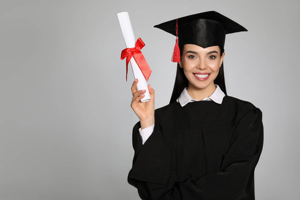灰色の背景に卒業帽子と卒業証書を持つ幸せな学生。テキストのスペース - 写真・画像