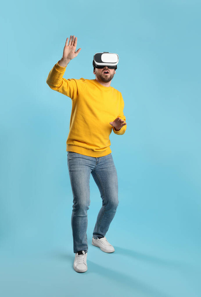 Emotional man using virtual reality headset on light blue background - Photo, Image