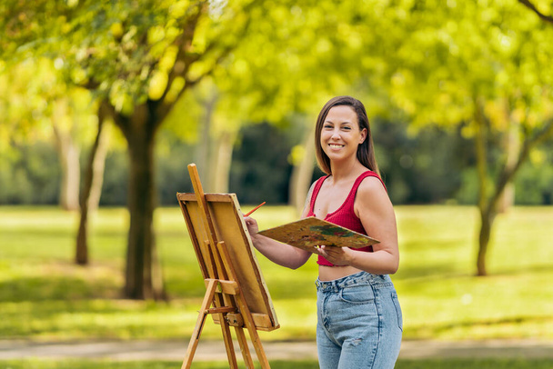 Женщина в летней одежде рисует на холсте на открытом воздухе - Фото, изображение