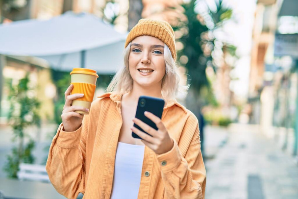 Mladá blondýna dívka pomocí smartphone a pití kávy ve městě. - Fotografie, Obrázek