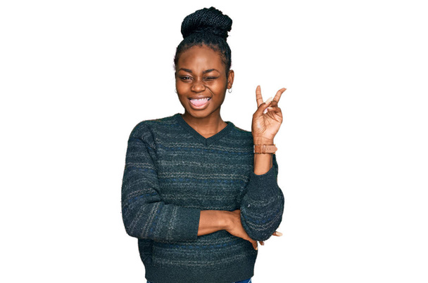 カジュアルな服を着た若いアフリカ系アメリカ人女性が、勝利のサインをしてカメラに顔をウィンクして微笑んでいる。2番.  - 写真・画像