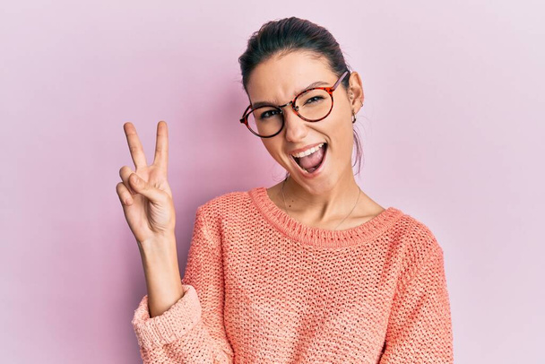 Young caucasian woman wearing casual clothes and glasses smiling with happy face winking at the camera doing victory sign. number two.  - Fotografie, Obrázek