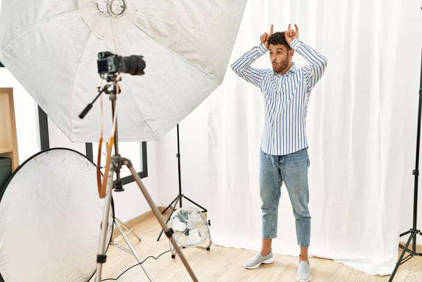 Арабский молодой человек, изображающий из себя модель в фотостудии, делает смешной жест с пальцем над головой, как рога быка  - Фото, изображение