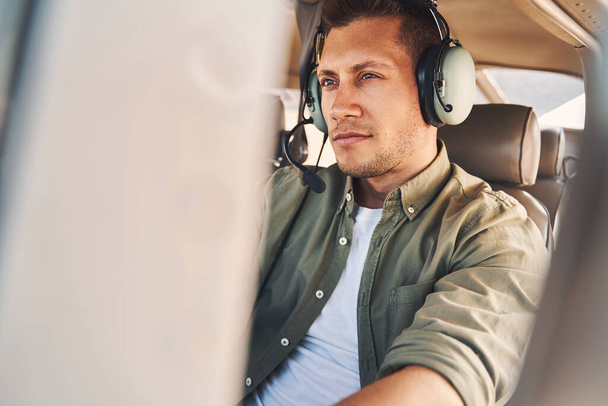 Handsome young man sitting in aircraft pilot cabin - Foto, Imagen