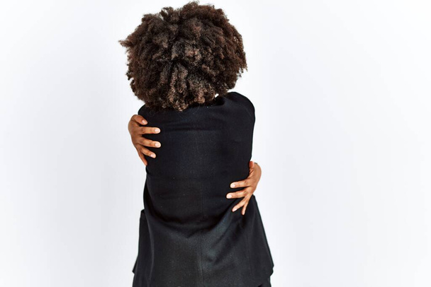 African american woman with afro hair wearing business jacket and glasses hugging oneself happy and positive from backwards. self love and self care  - 写真・画像